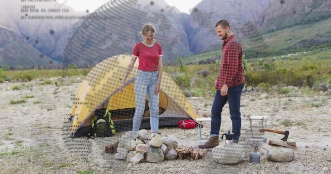 Couple building campfire in mountain valley near yellow dome tent, with axe and camping table - Powered by Adobe