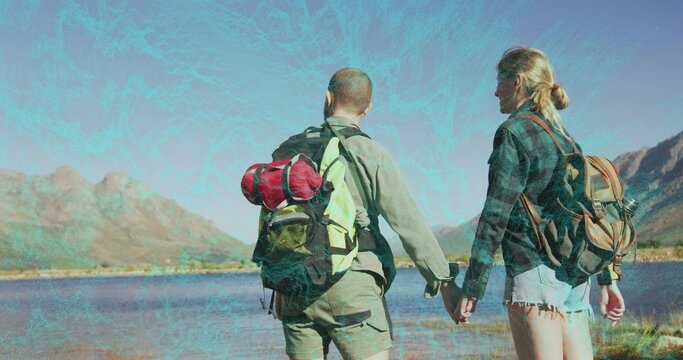 Standing hiking couple holding hands at grassy lakeshore, with backpacks and red sleeping bag - Powered by Adobe