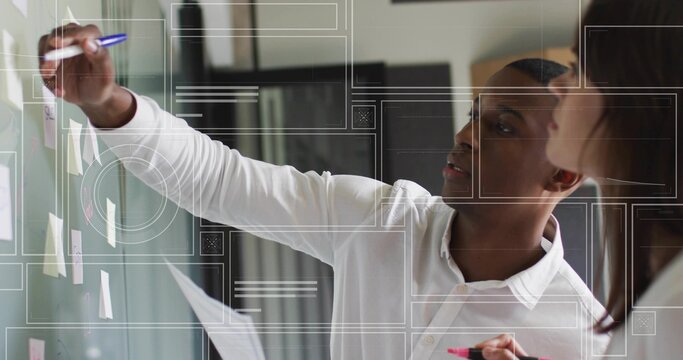 Collaborating business professionals writing on glass board at office with sticky notes and markers