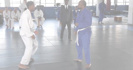 Sparring two martial artists wearing white and blue gis facing off in dojo, with padded mats