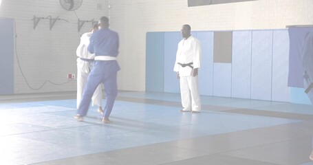 Instructor guiding students grappling on interlocking mats in training studio, with gis and belts