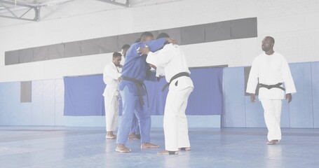 Grappling pair locking in clinch on dojo blue mats, with judo gis and black belts