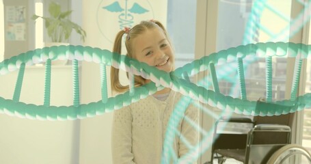 Smiling girl in sweater standing in clinic with wheelchair, caduceus poster, DNA helix overlay