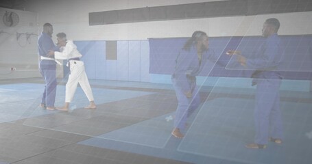 Practicing four martial artists grappling drills inside gym, with gis, belts, mats, panels and fan