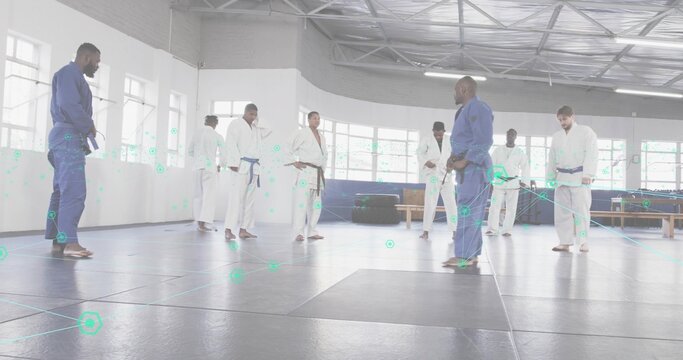 Instructor in blue gi leading group on mats inside training hall, with windows, copy space
