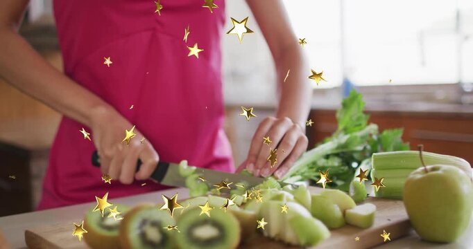 Woman slicing kiwi on kitchen cutting board, revealing celery and apple stars twinkling for cooking