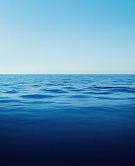 Fototapeta premium Deep blue ocean water gently moving, creating a serene, minimalist scene with a clear light blue sky above the horizon