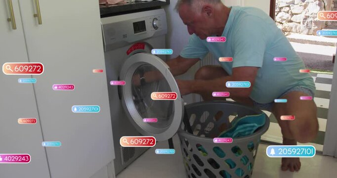 Senior man crouching at washer opening drum door loading laundry for home pulling white towels - Powered by Adobe