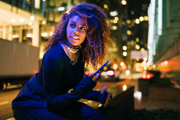 Young woman using smartphone sitting in city at night