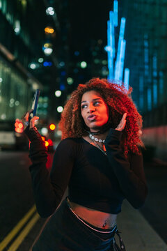 Influencer posing at night with smartphone and colorful lights 