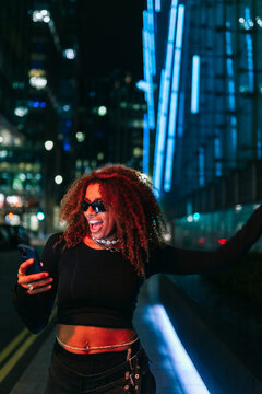 Excited young woman using phone in urban environment at night