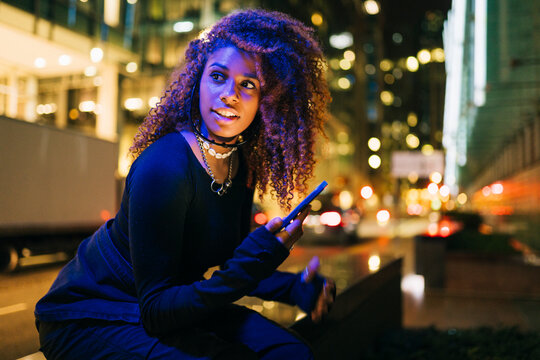 Young woman using smartphone sitting in city at night