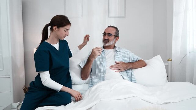 young nurse in uniform takes care of an elderly man, holding his hand and asking him about his condition and giving him encouragement. A nurse uses a stethoscope to check his pulse in a nursing home.
