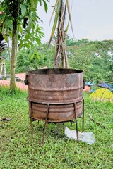 Old rusty metal barrel stands on the grass in the garden on a cloudy day