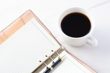 コーヒーとシステム手帳、ボールペンでデスクワークをしているイメージ
