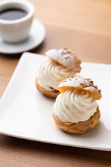Cream puffs with whipped cream and a cup of coffee on a wooden table