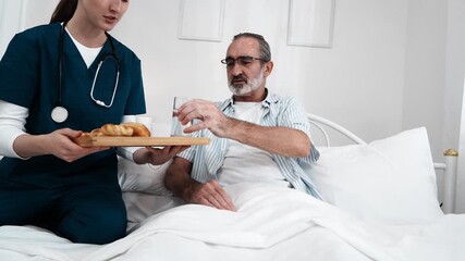 An elderly man sits on a bed while a nurse serves breakfast and gives the sick person milk to drink to take care of their health in a nursing home.
 - Powered by Adobe