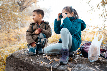 Young siblings exploring nature looking through binoculars in autumn