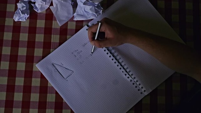 An overhead shot captures a student's hand diligently working through difficult math equations in a spiral notebook.