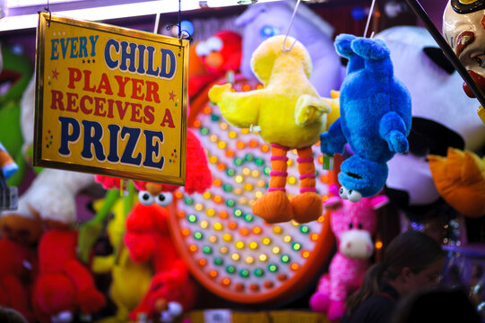 Sideshow Alley at a fair showing a sign saying "every Child Wins A Prize" with stuffed toy prizes hanging around it - horizontal
