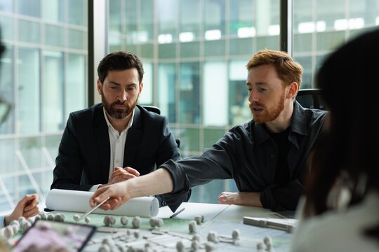 Red hair architect showing model of new residential area to colleagues