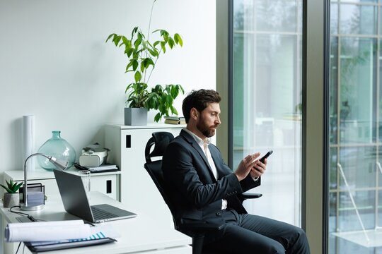 Focused male office employee typing mobile phone on office chair