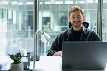 Portrait of smiling office worker at desk with open laptop in office