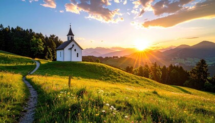 Small white church on a grassy hill at golden hour sunset with sun rays over distant mountains and trees