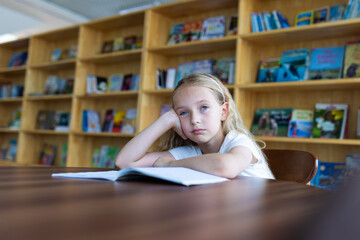 Young girl looking bored while studying in a library