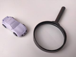 The image shows a small, purple toy car next to a magnifying glass