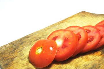 Fresh red tomato slices, solanum lycopersicum or lycopersicum esculentum on an old wooden cutting board photographed on the isolated white background
