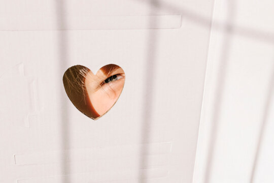 Naklejki Child’s eye peeking through heart-shaped cutout in cardboard