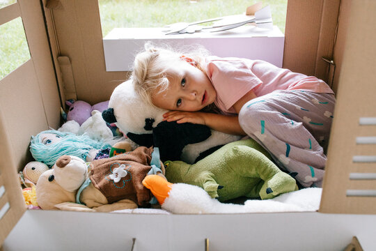 Child resting with stuffed animals inside a cardboard playhouse