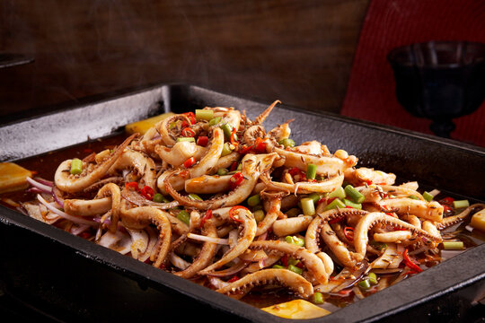 Spicy braised squid tentacles in a wok, close-up.