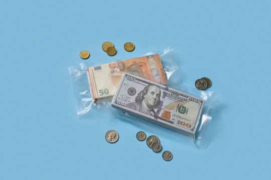 Money in vacuum bags with dollar, euro, coins on blue