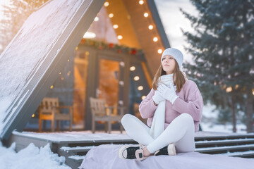 Cozy winter moment of a young woman enjoying the snowy outdoors in front of a charming cabin at sunset