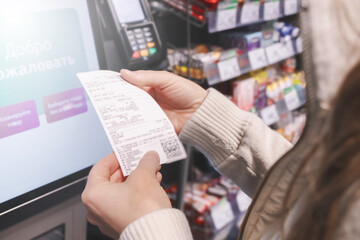 A woman checks her shopping receipt at a self-service checkout in a store, focusing on her expenses and family budget while using the touchscreen interface.