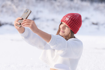 Young woman in a red hat takes a selfie in a snowy landscape during a bright winter day