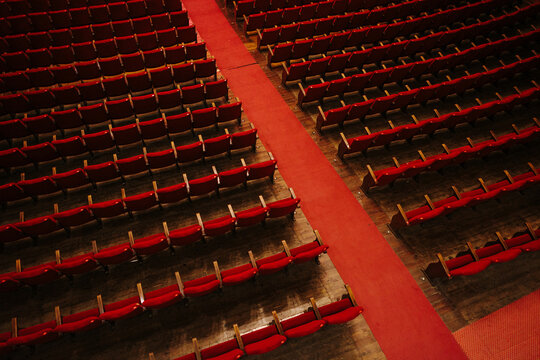 Red carpet dividing rows of empty red chairs in theatre or auditorium