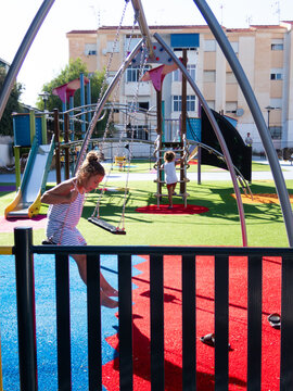 Girl swinging on a swing in a playground while another girl
