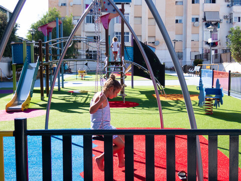 Girl swinging on a swing in a playground with colorful rubber flooring