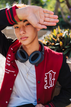 Young man shields eyes, wearing headphones and jacket.