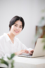 관엽식물의 푸르름이 있는 방에서 컴퓨터를 하는 여성의 카메라를 응시하는 모습 주부나 디자이너의 원격 근무나 재택 근무 등의 이미지