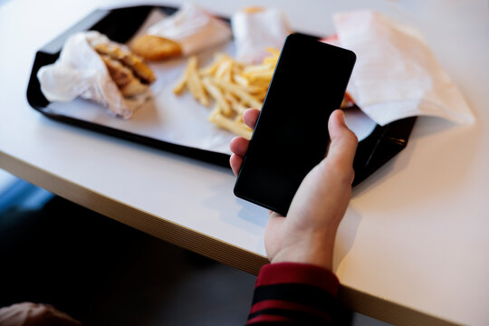 Phone in hand, fast food on tray.