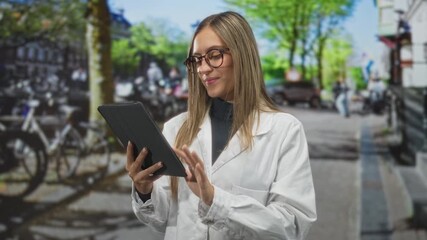 Woman holding tablet reaches out on a busy city street with bicycles and parked cars, wearing white coat and glasses; digital confidence.