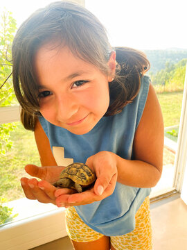 Young Girl Joyfully Holding a Tortoise in a Sunny Garden Setting