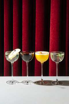 Four assorted cocktails in stemmed glasses against red curtain backdro