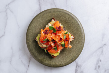 Gourmet toast with smoked salmon, roe, and herbs on green plate
