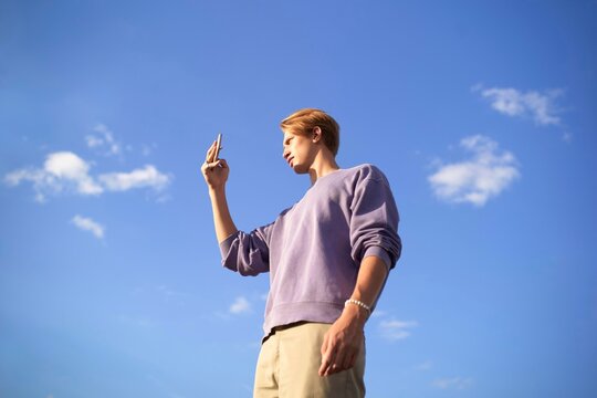 Young Man Taking a phone photo Under a Bright Blue Sky