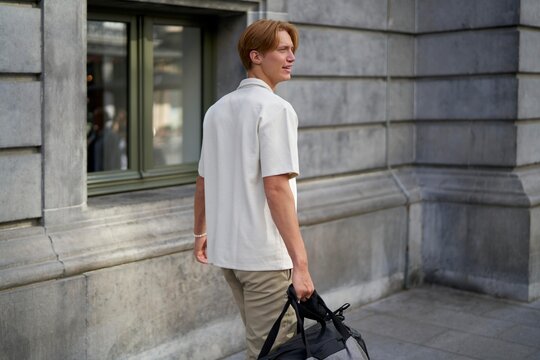 Young Man Walks Along City Street Carrying a Duffel Bag